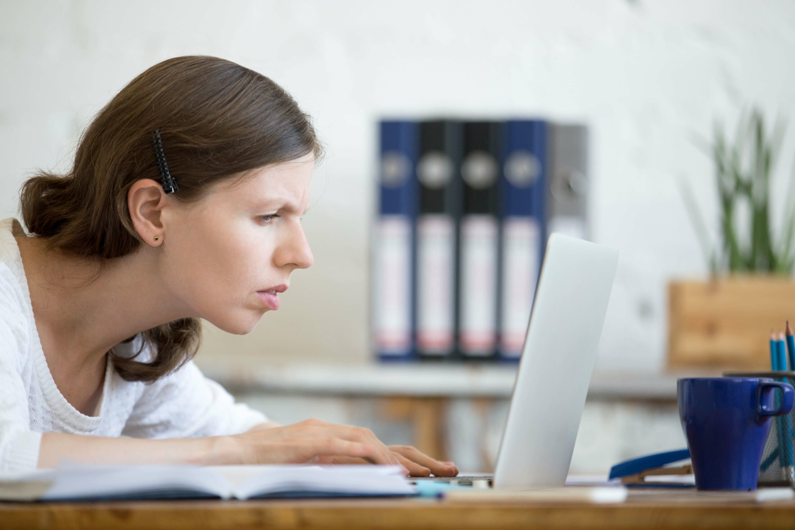 A woman that is sitting in front of her computer is looking to close at the screen