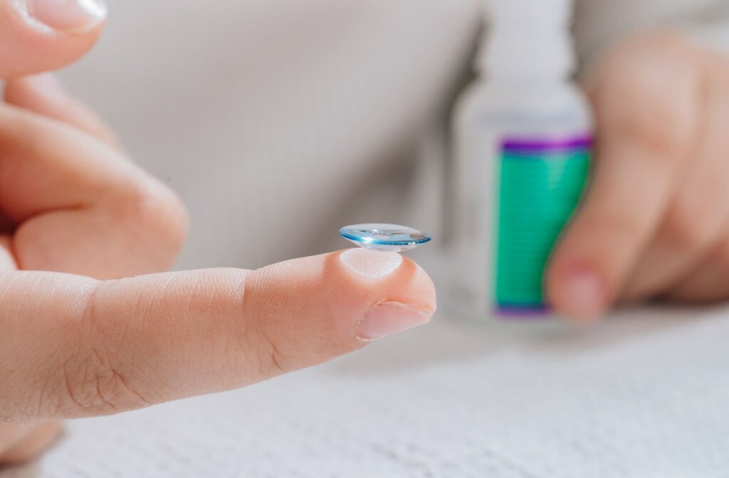 A child holds a contact lens on their index finger, while holding a bottle of contact lens solution in the other hand.