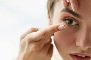 A close up image of a woman placing a contact lens into her right eye