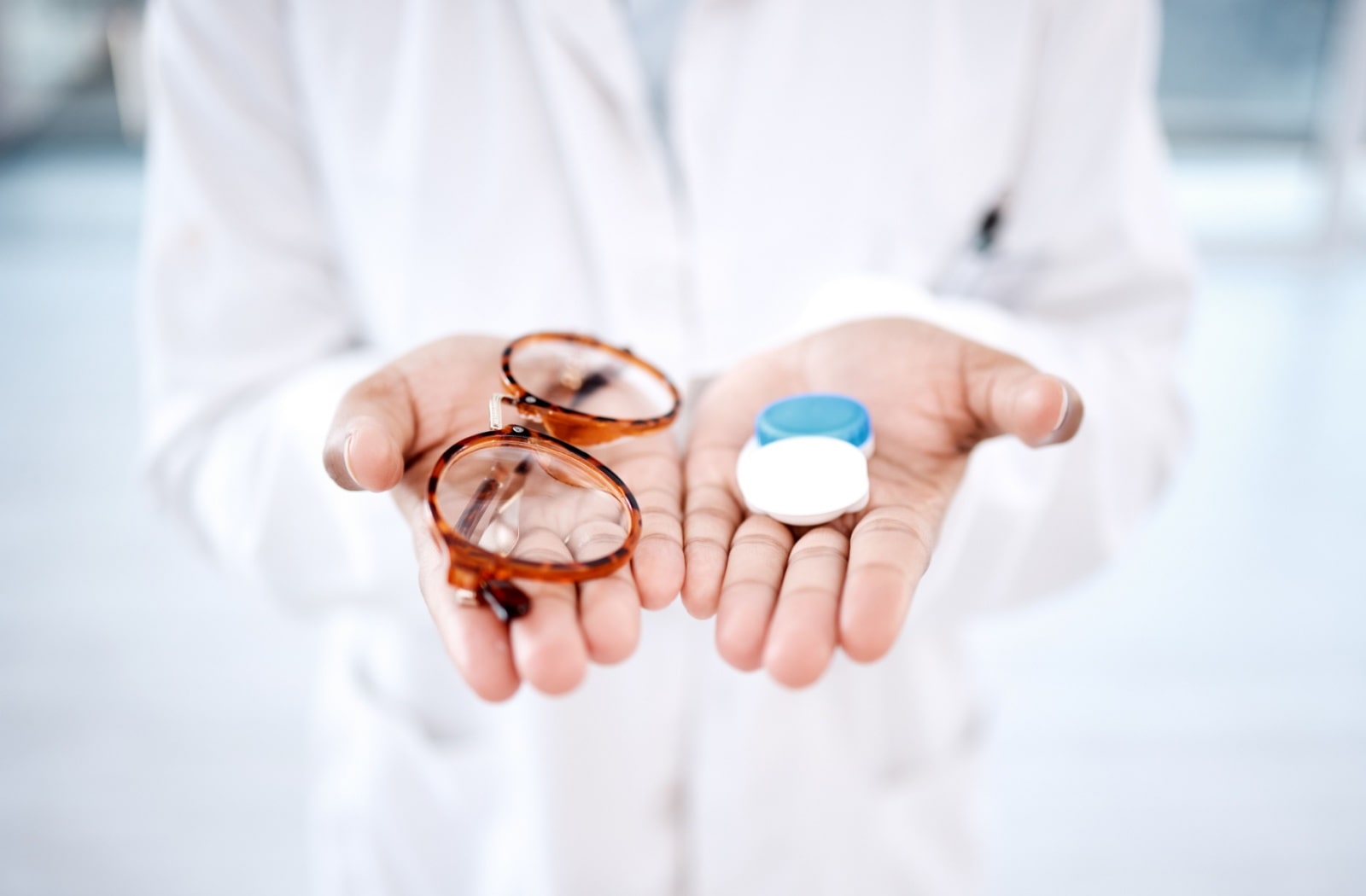 An optometrist holding out their hands, with a pair of glasses in one hand and a contact lens case in the other