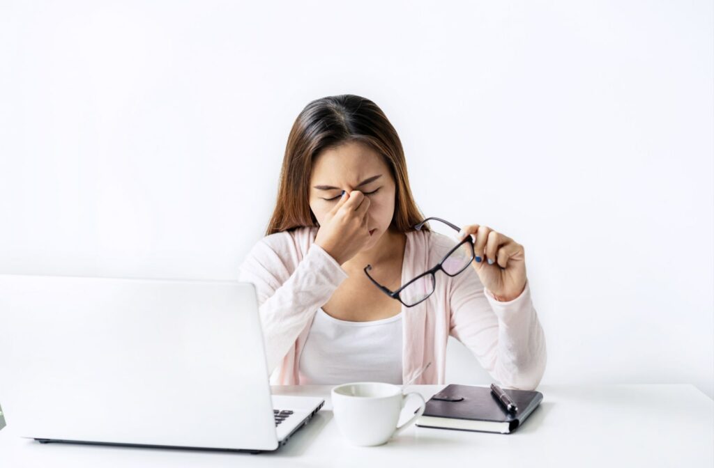 A woman sitting at a desk with her laptop while rubbing her eyes due to eye strain