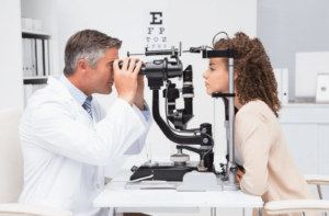 A male optometrist examines a female patient's eyes in an optometry office.