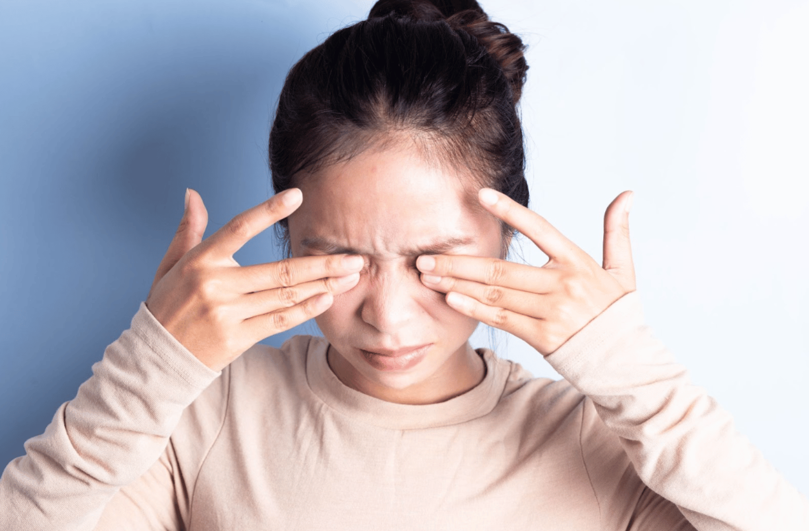 A young woman rubbing her eyes in frustration due to dry eye syndrome.