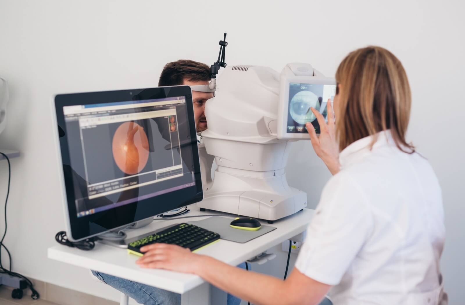 A female optometrist at her desk examining a digital image of a male patient's retina.