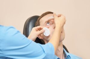 An eye doctor applying eye drops to a patient to diagnose dry eye disease.