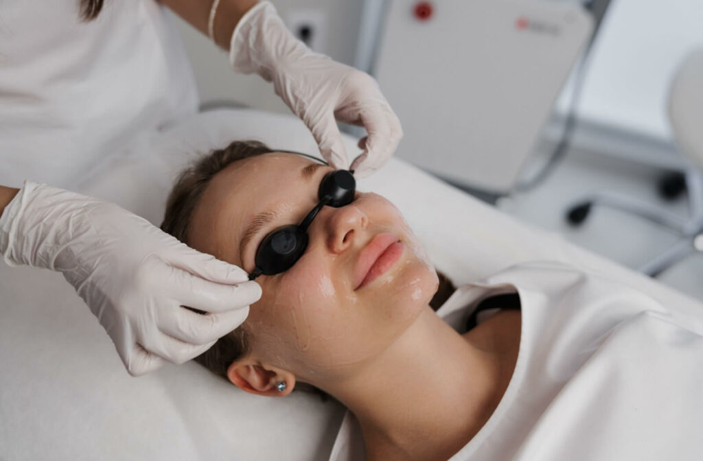 An eye doctor placing protective eyewear over a woman's face before starting IPL therapy.