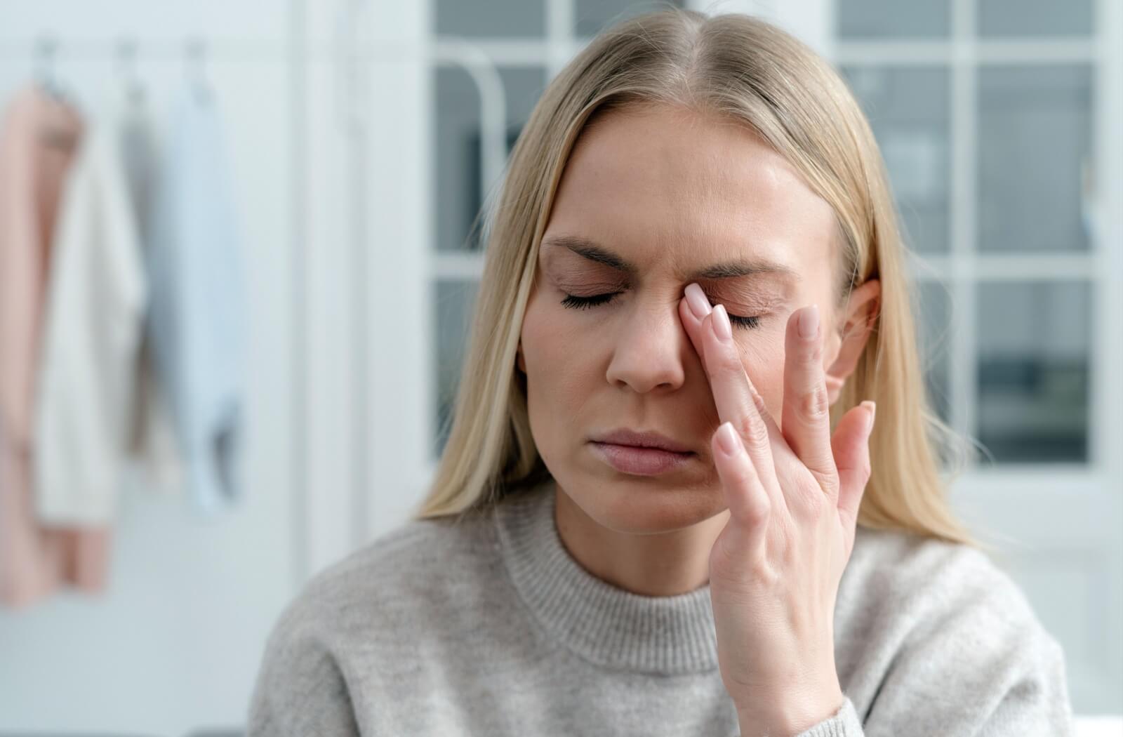 A patient rubbing their eye with their left hand in frustration due to waking up with dry eyes.