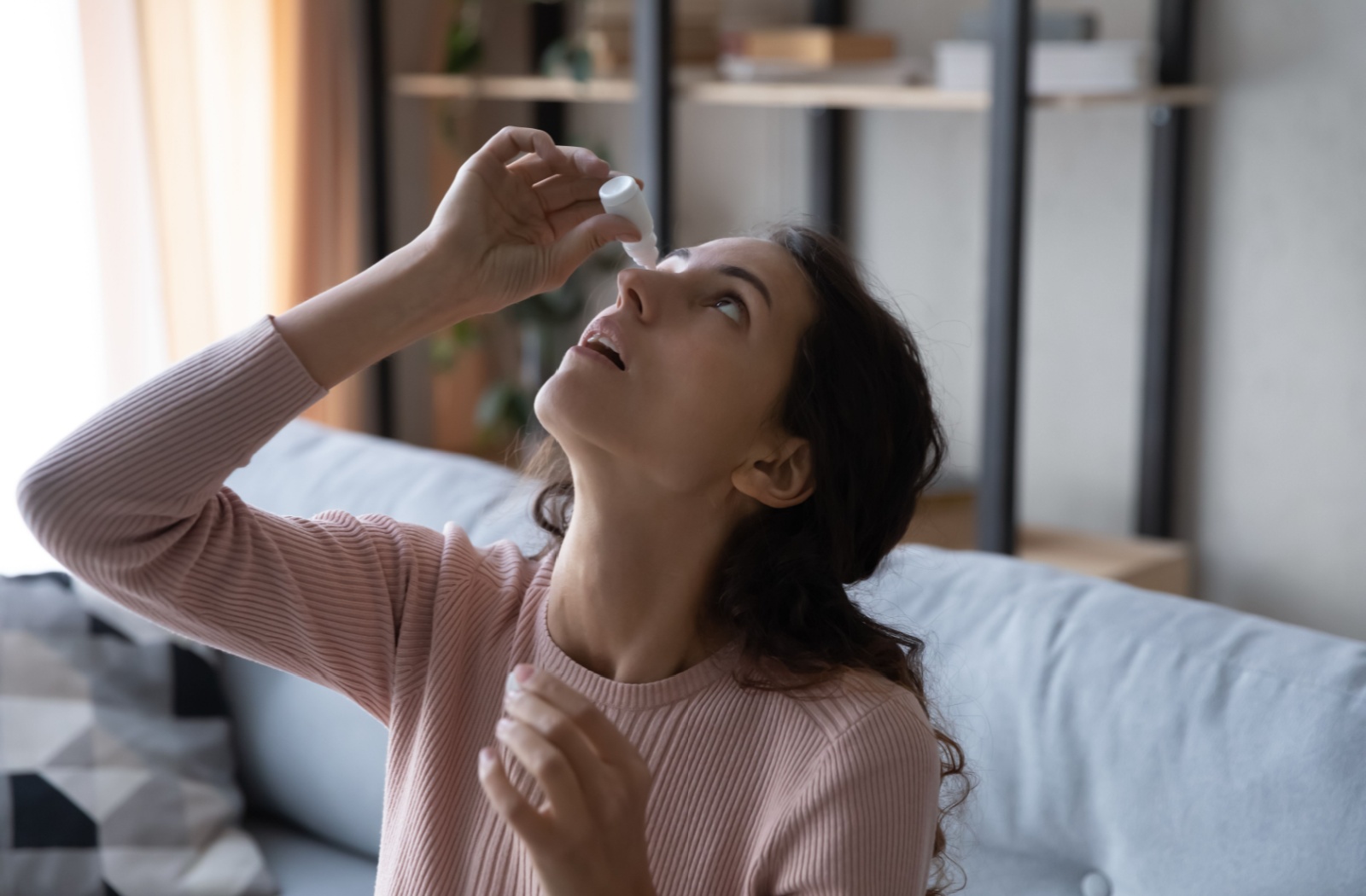 Woman tilting her head back while applying eye drops to her eye.