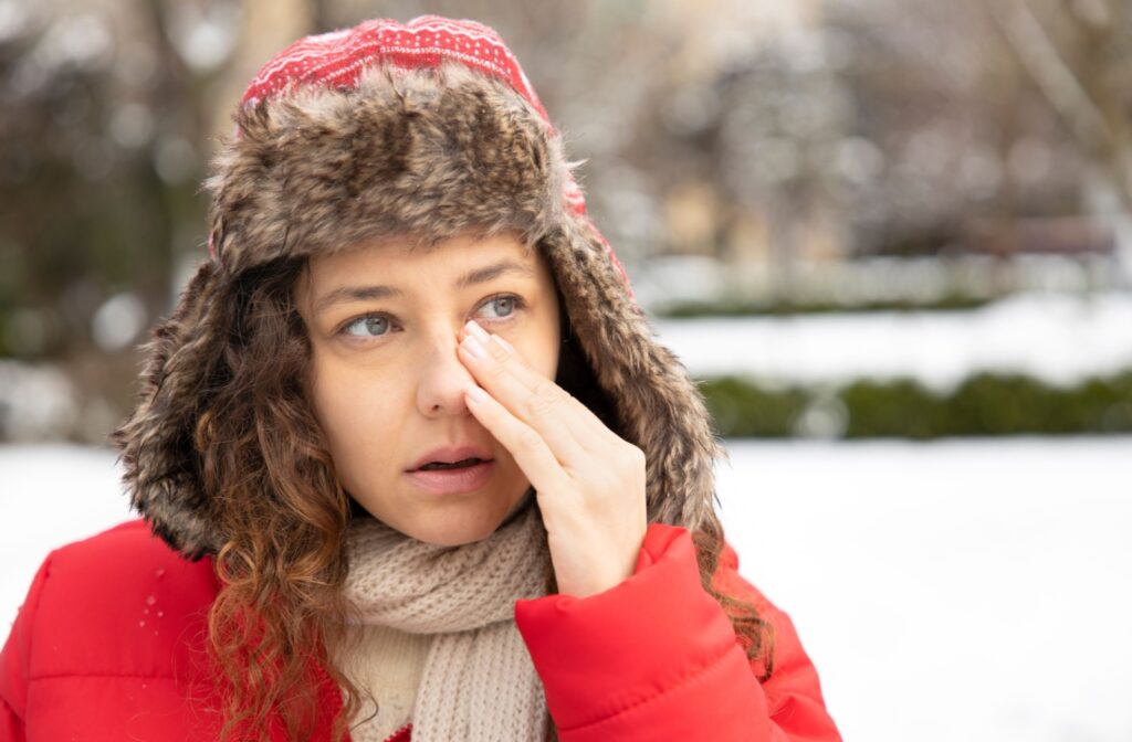 Woman in winter clothes rubbing her watery eye outdoors.