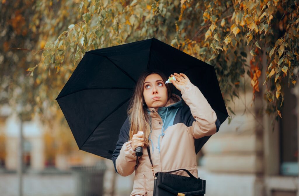 Woman under an umbrella applying eye drops in cold weather.