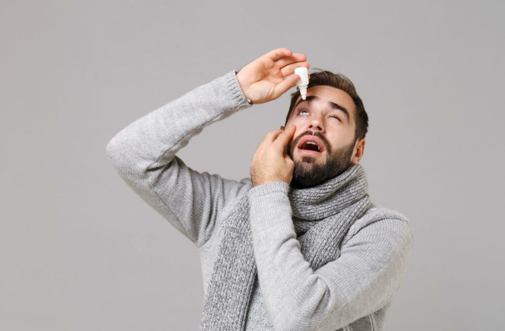 A patient wearing all gray is applying eye drops.