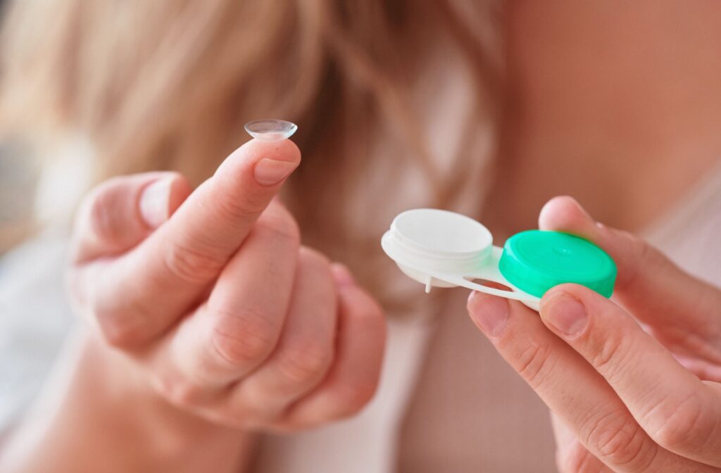A close-up of a person holding a contact lens on their fingertip with a contact lens case in the other hand. 