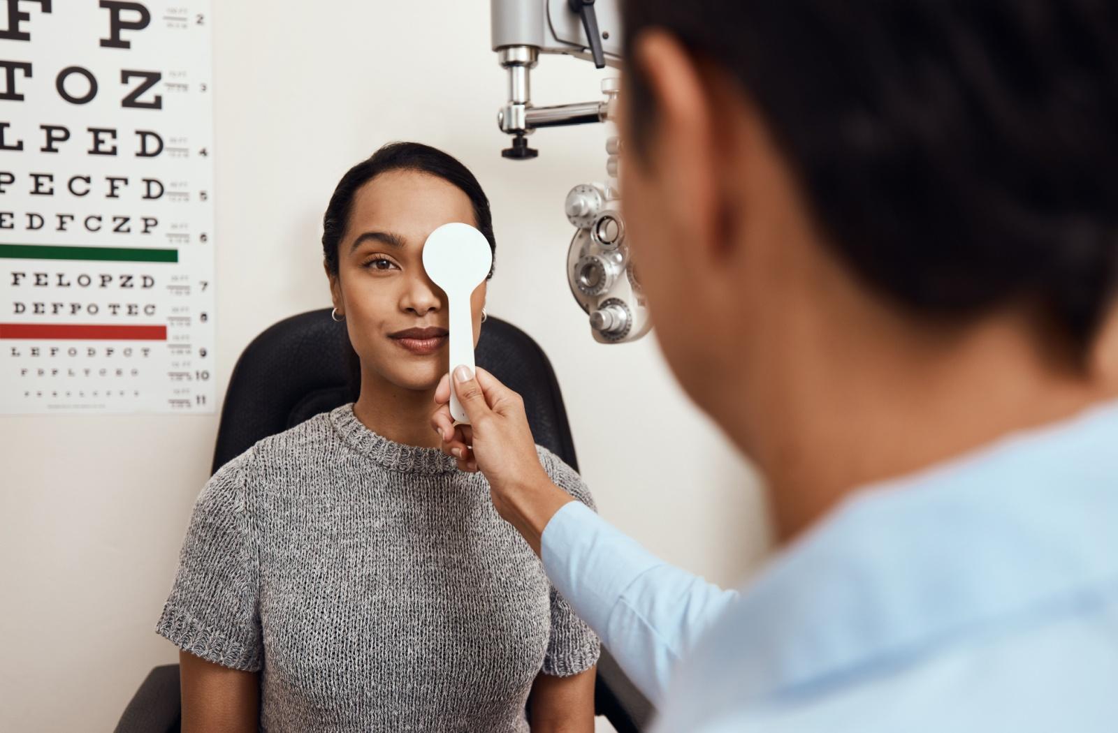 Eye doctor covering one of a patient’s eyes during a vision exam in an optometry clinic.