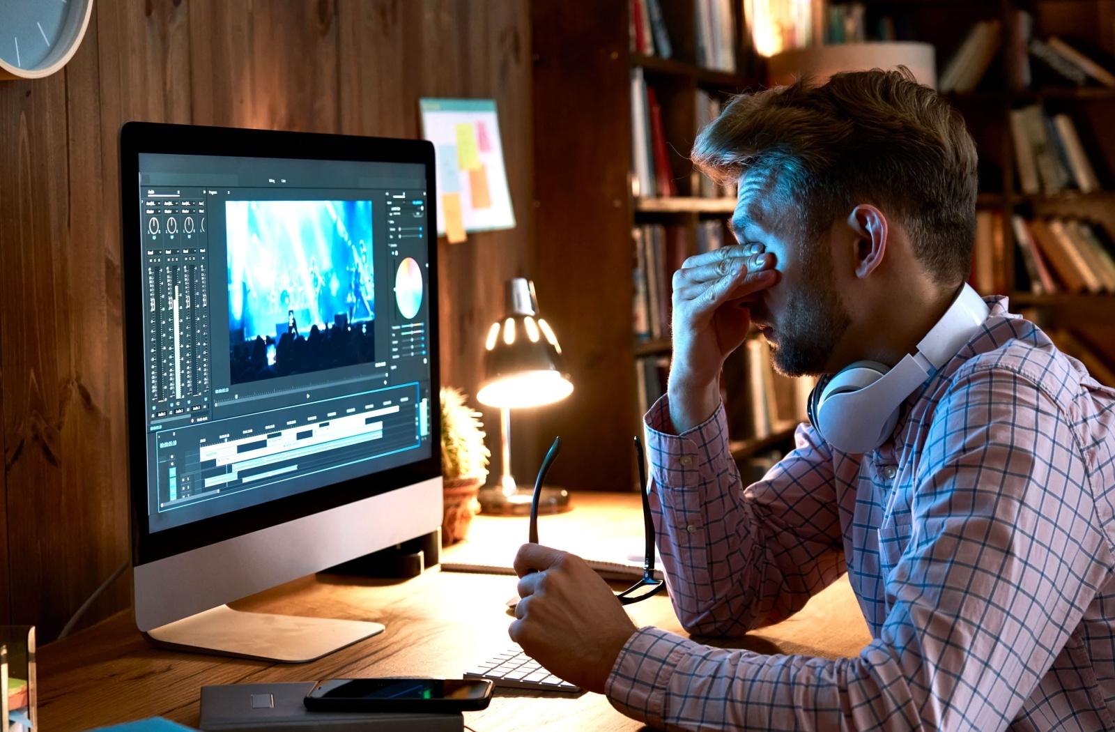 Man experiencing eye strain while working on a computer in a dimly lit room.