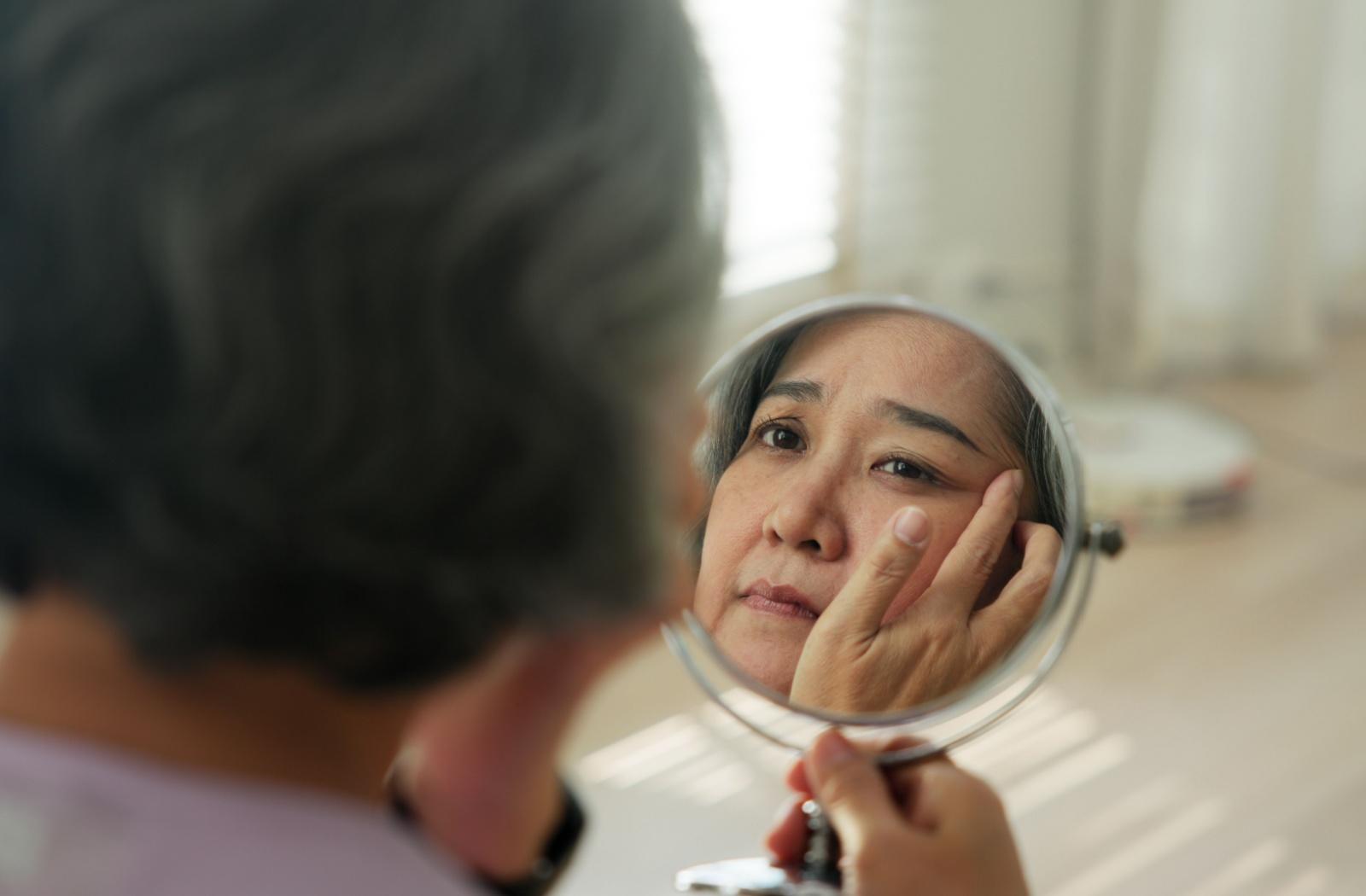 Older woman looking closely at her eye in a mirror while checking for changes in her vision or eye health