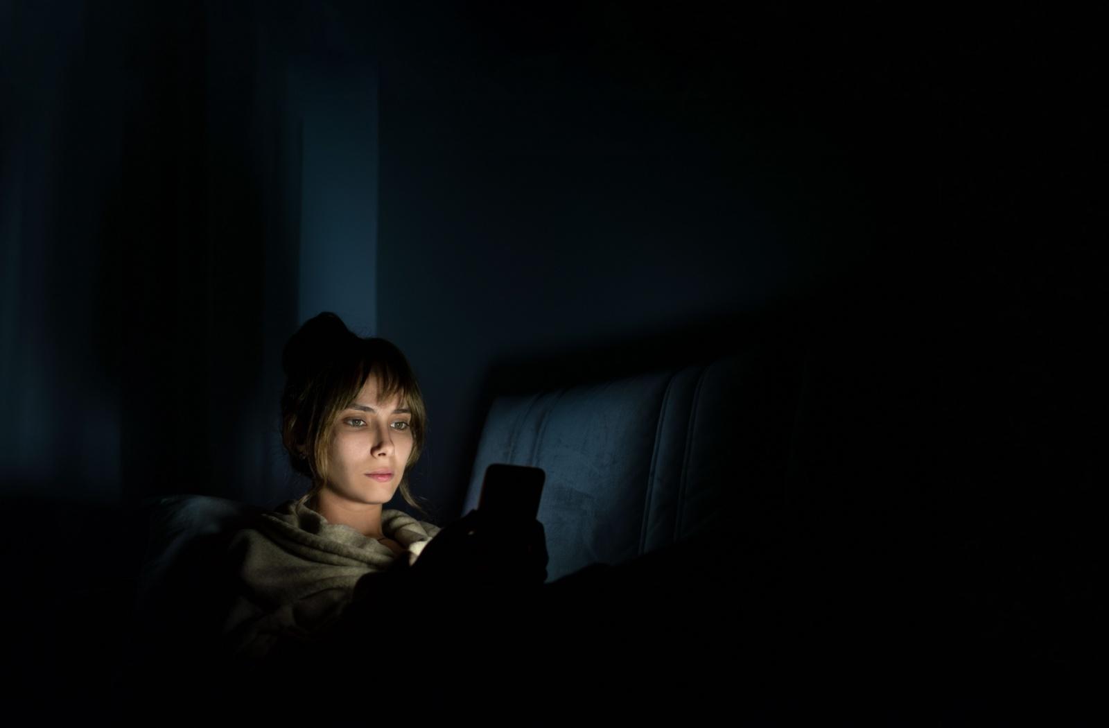 Person using a smartphone in a dark room with screen light illuminating their face.